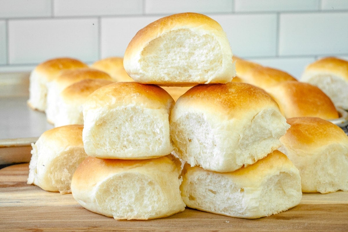 Stack of dinner rolls on wooden cutting board.