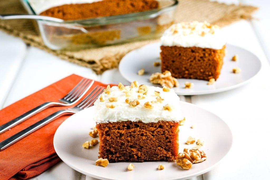 Two slices of pumpkin cake with cream cheese frosting on white plates.