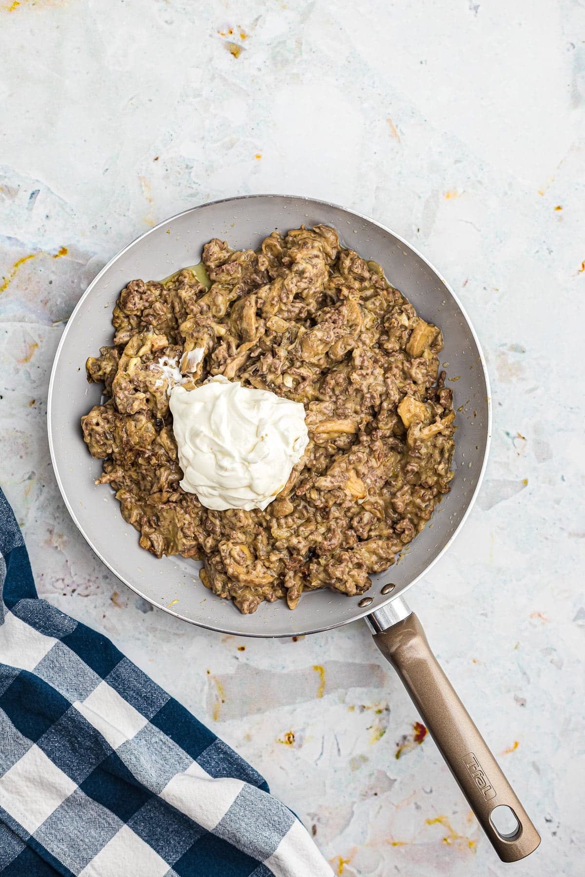 Skillet with sour cream on top of stroganoff before mixing.