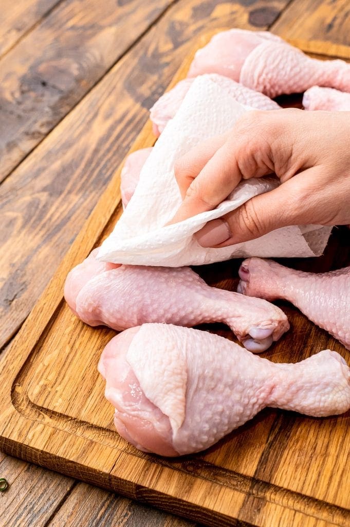 Hand patting chicken legs with paper towel before baking