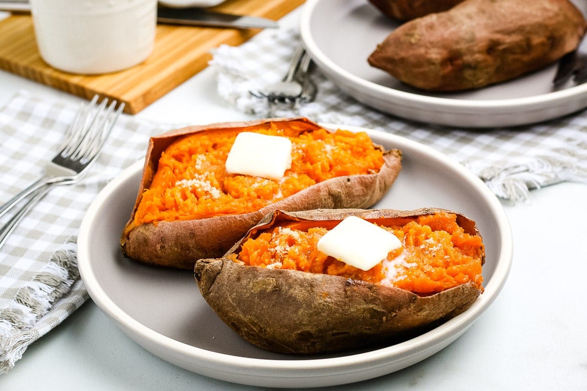 White plate with two sweet potatoes cut open and butter on top