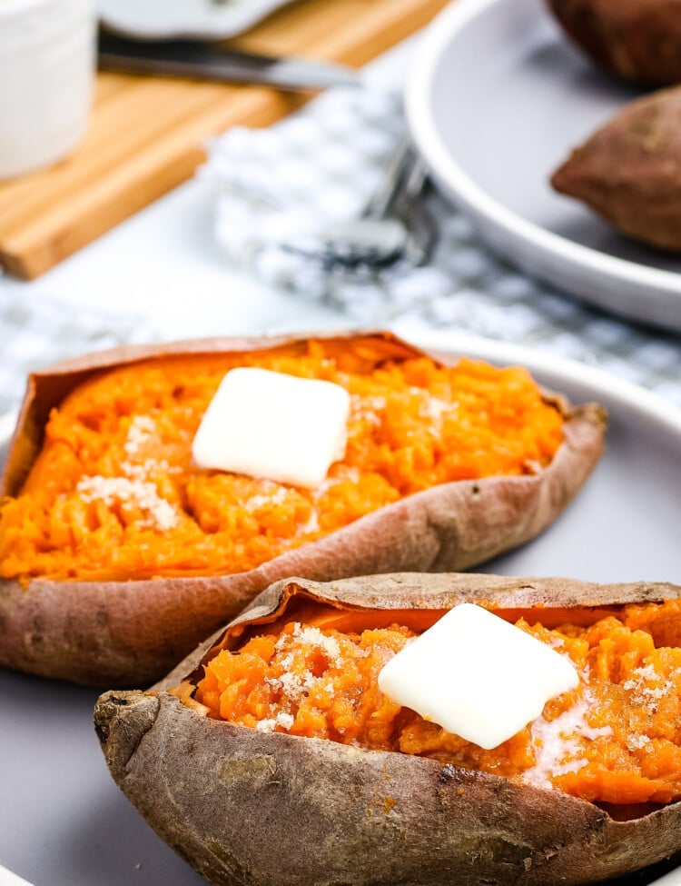 White Plate with two sweet potatoes with a slab of butter on top of each one.