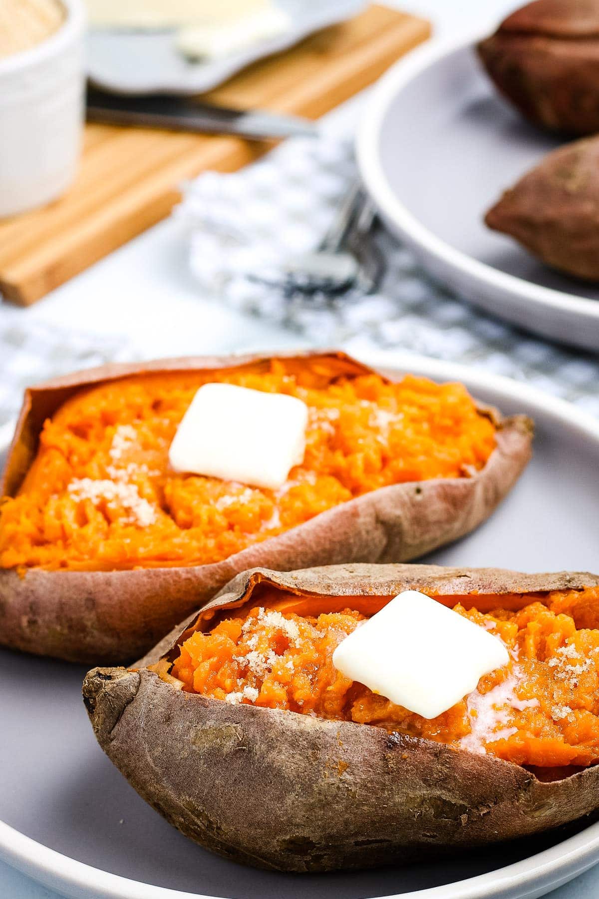 White Plate with two sweet potatoes with a slab of butter on top of each one.