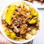 Hand holding Mississippi Pot Roast in bowl over mashed potatoes.
