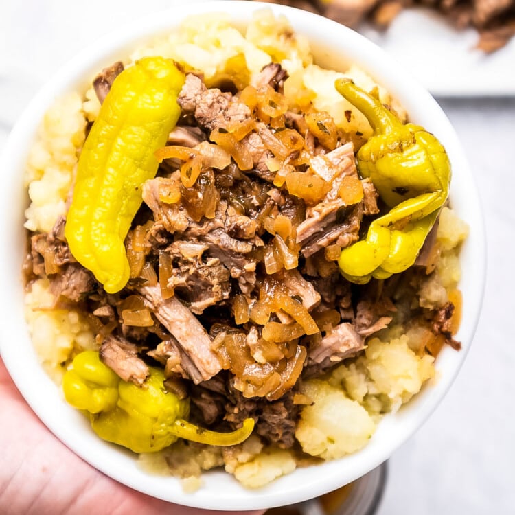 Hand holding Mississippi Pot Roast in bowl over mashed potatoes.
