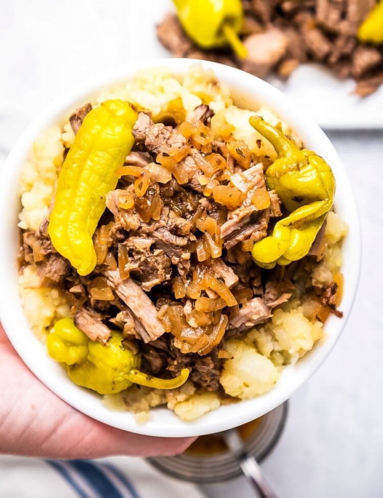 Hand holding Mississippi Pot Roast in bowl over mashed potatoes.