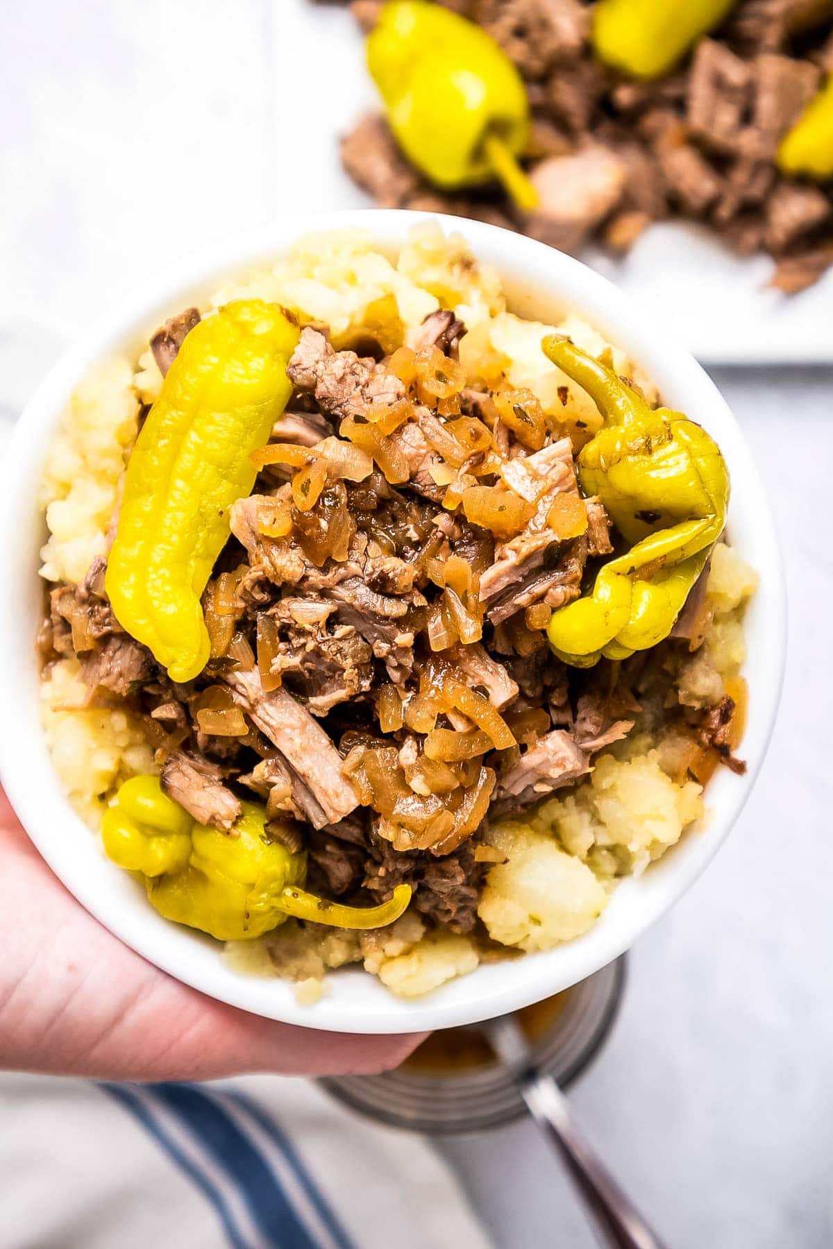 Hand holding Mississippi Pot Roast in bowl over mashed potatoes.