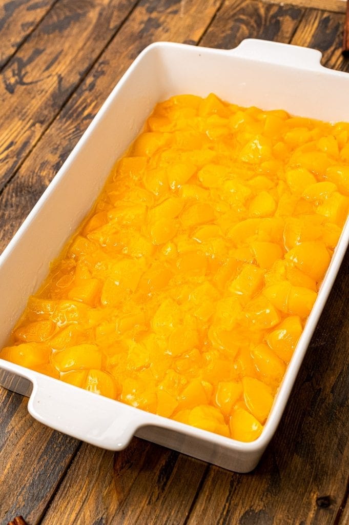 White baking dish with peach pie filling spread out on bottom