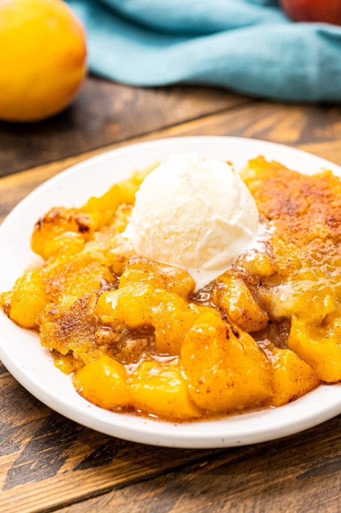 White plate with peach dump cake on it topped with ice cream.