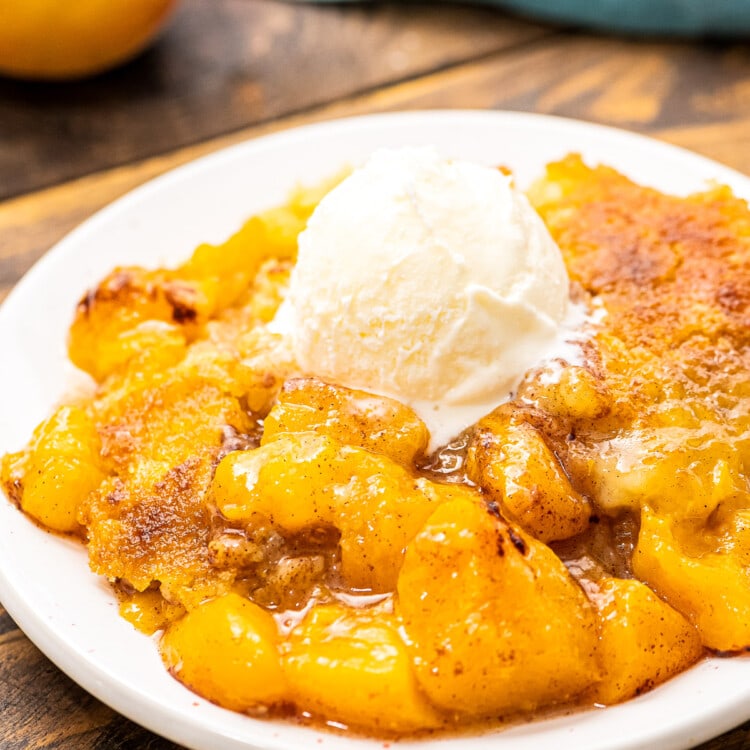 White plate with peach dump cake on it topped with ice cream.