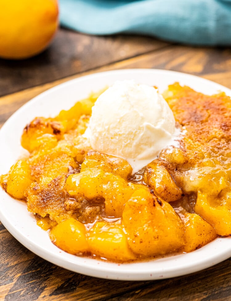 White plate with peach dump cake on it topped with ice cream.