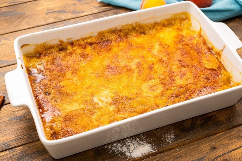 Landscape image of a baked peach dump cake in white baking dish.