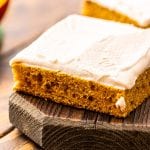 Square Slice of Pumpkin Bars with Cream Cheese Frosting on a wooden cutting board