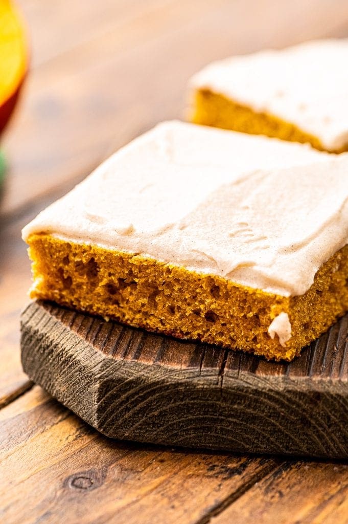 Square Slice of Pumpkin Bars with Cream Cheese Frosting on a wooden cutting board