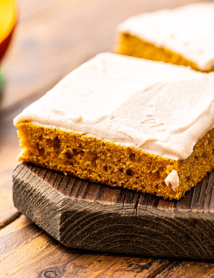 Square Slice of Pumpkin Bars with Cream Cheese Frosting on a wooden cutting board