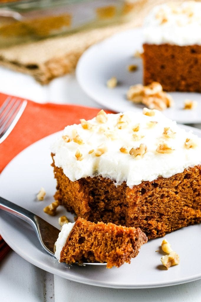 Slice of pumpkin cake on white plate with a fork laying next to it with a bite out of it.