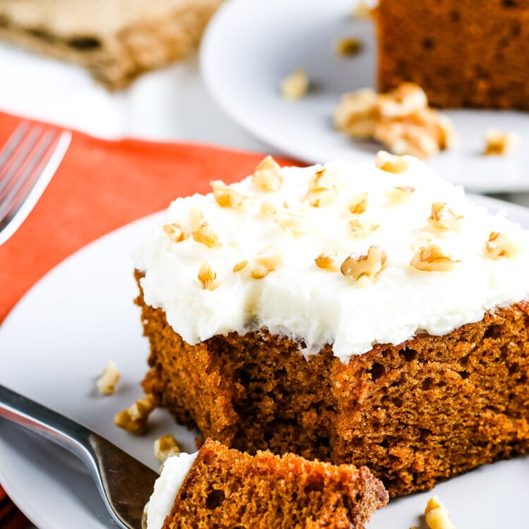 Slice of pumpkin cake on white plate with a fork laying next to it with a bite out of it.