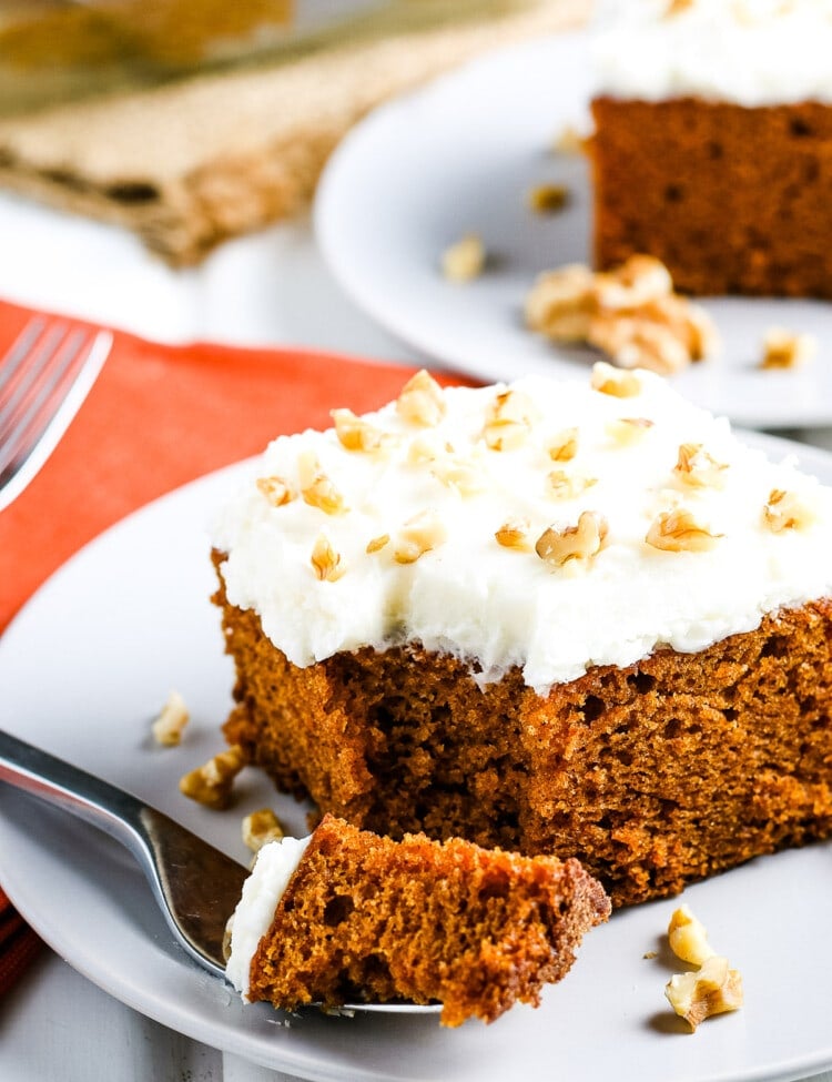 Slice of pumpkin cake on white plate with a fork laying next to it with a bite out of it.