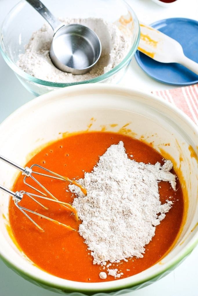 Hand mixer sitting by a bowl with pumpkin mixture and flour before mixing