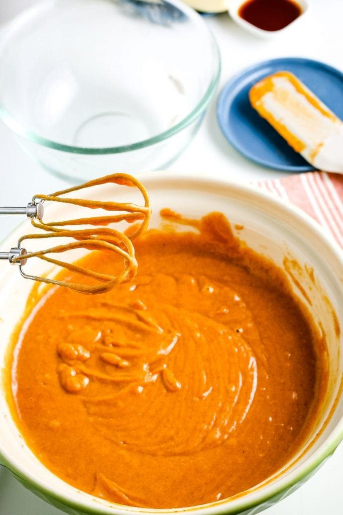 Bowl of mixed pumpkin cake batter with hand mixer sitting by it.