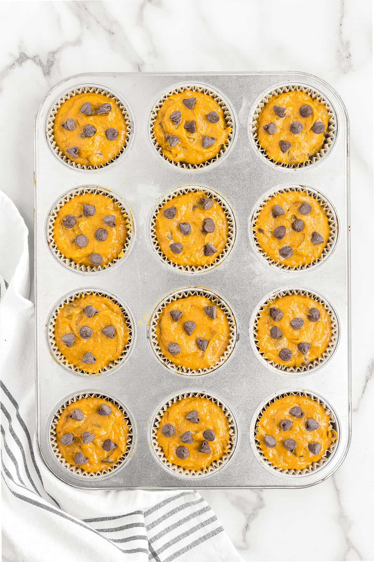 Muffin tin with pumpkin muffin batter and chocolate chips on top