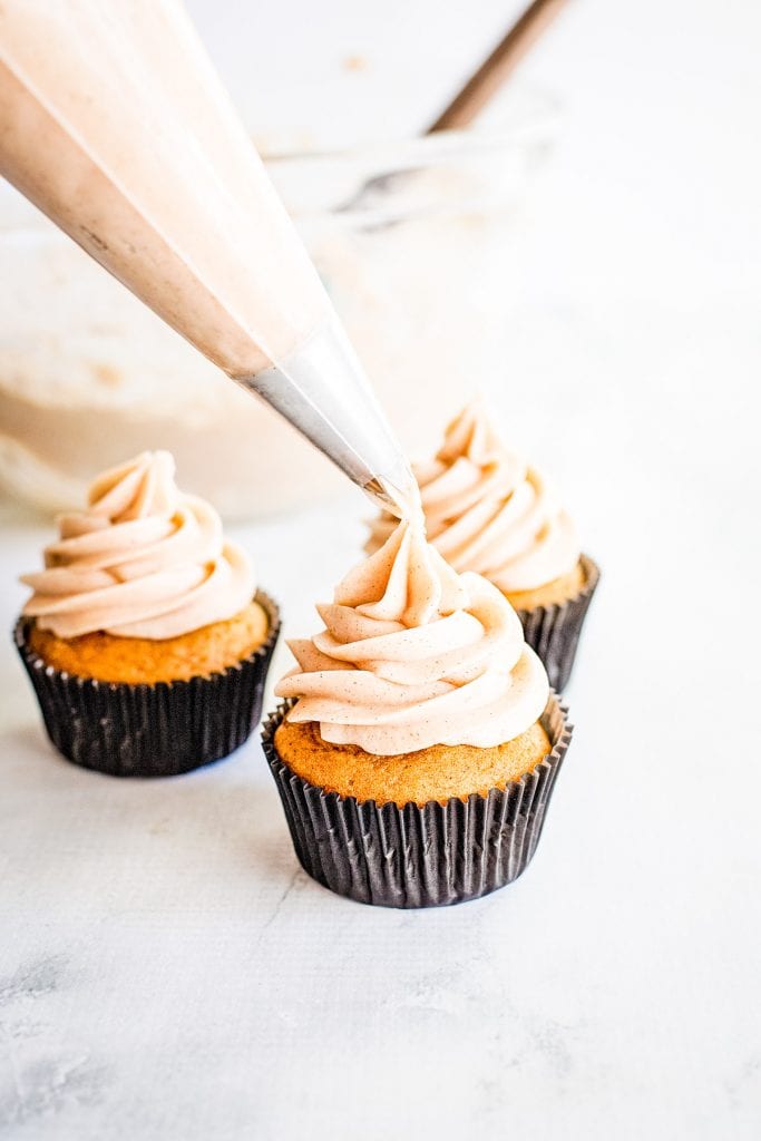 Piping bag with frosting being piped onto cupcake