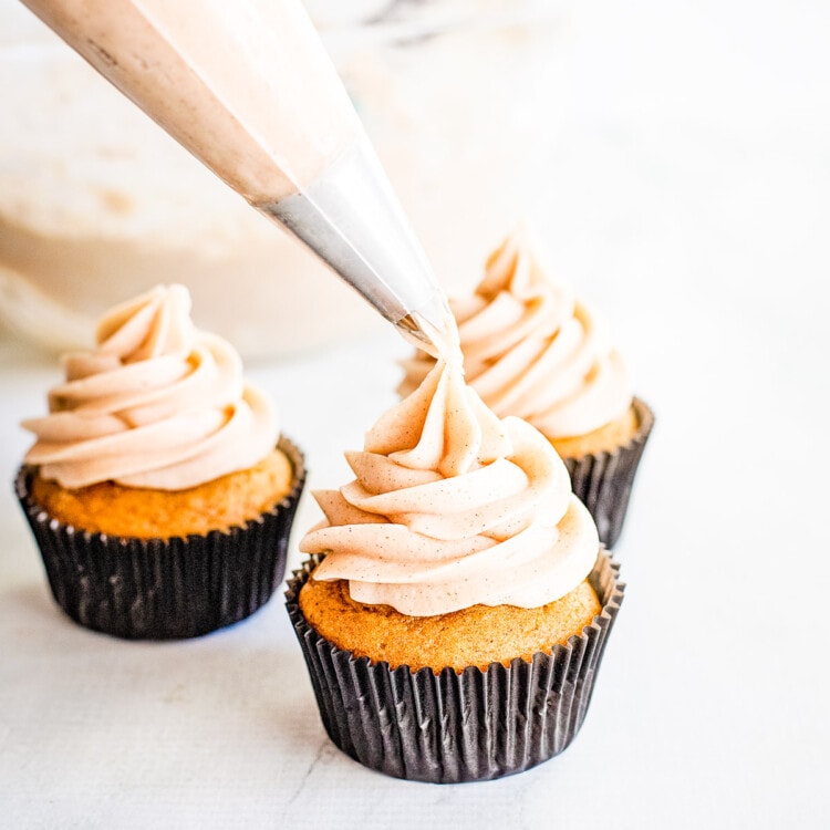 Piping bag with frosting being piped onto cupcake