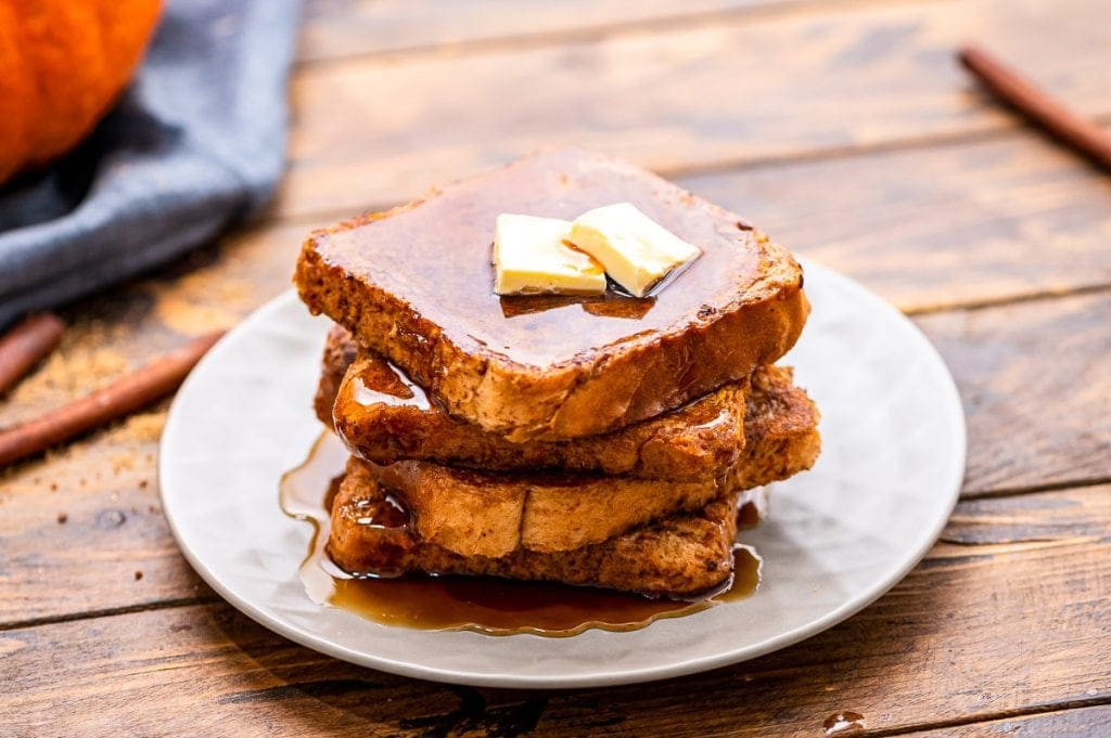 White plate with a stack of french toast on it topped with butter and syrup