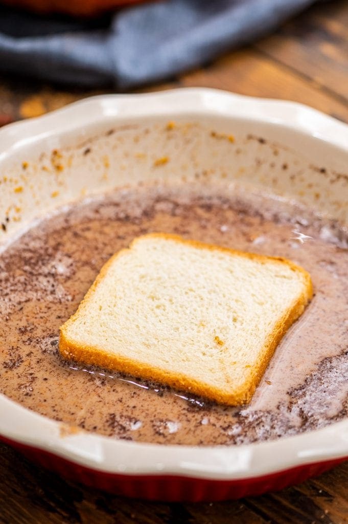 White pie plate with a piece of bread in french toast batter.