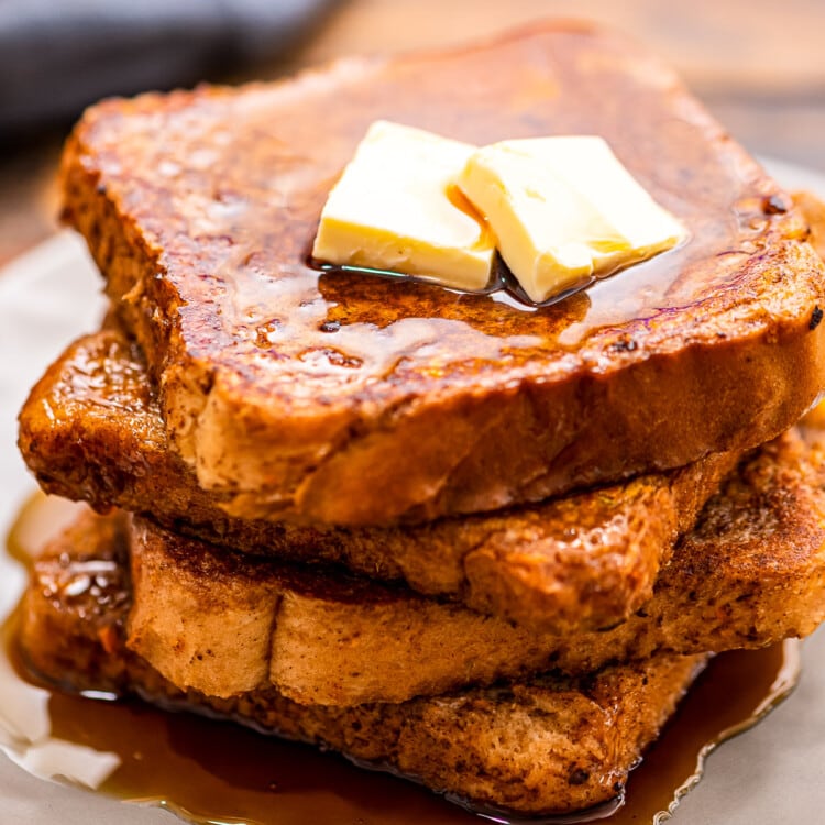A white plate with a stack of pumpkin french toast topped with butter and syrup