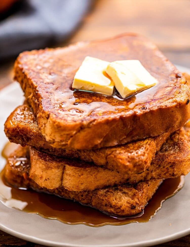 A white plate with a stack of pumpkin french toast topped with butter and syrup