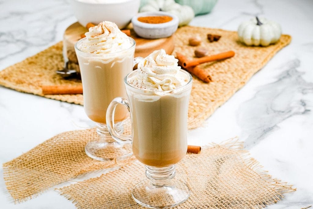 Pumpkin Spice Latte in tall glass mugs with whipped cream and cinnamon on top.