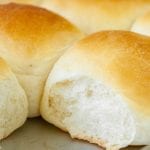 Close up image of dinner rolls on baking sheet with one roll missing in corner.