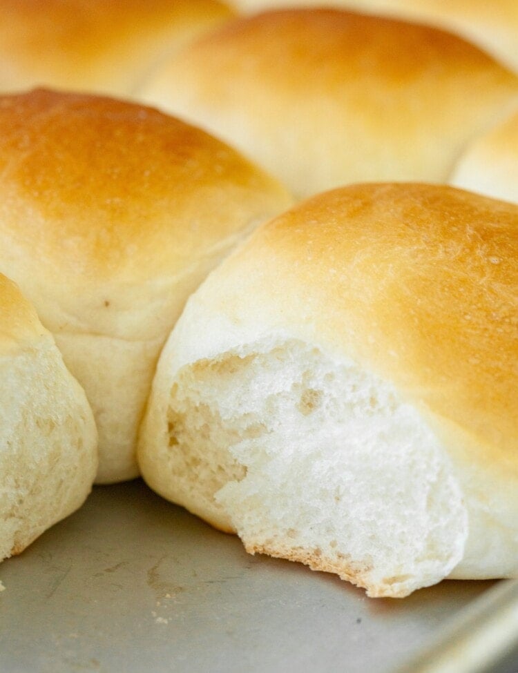 Close up image of dinner rolls on baking sheet with one roll missing in corner.