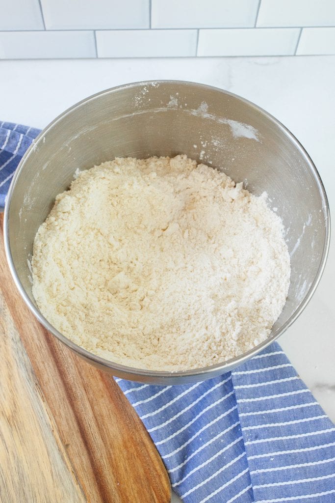 Metal mixing bowl with a crumbly mixture of shortening in flour after mixing