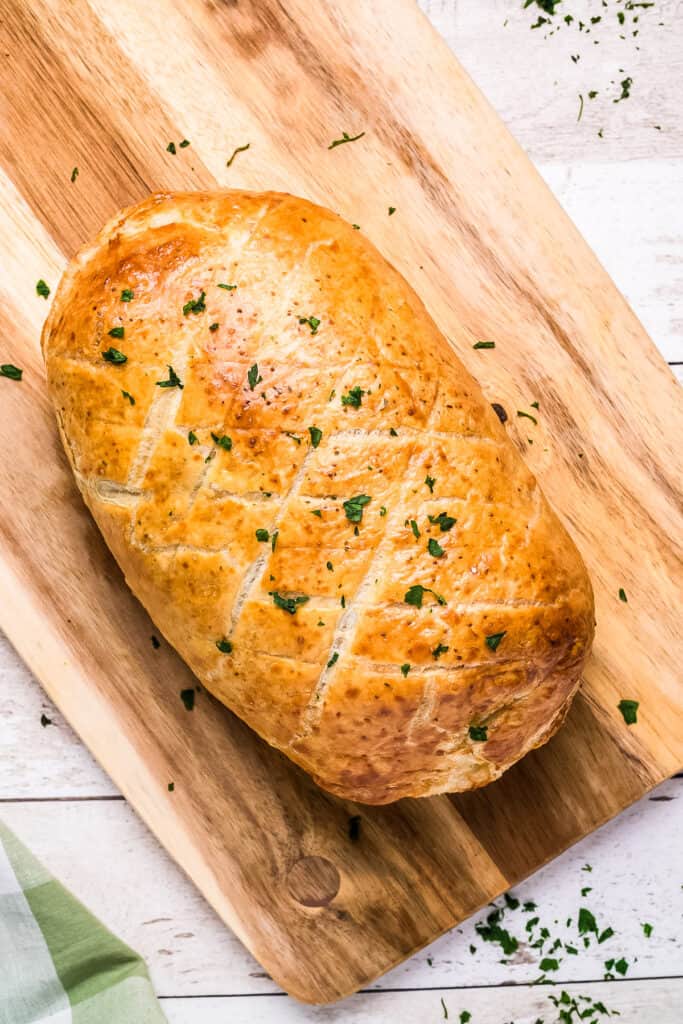 Whole cooked Beef Wellington on wood cutting board