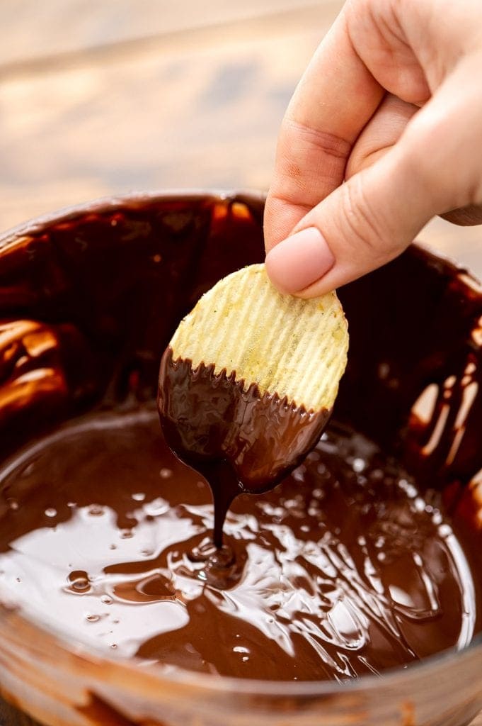 Hand dipping potato chips in chocolate.