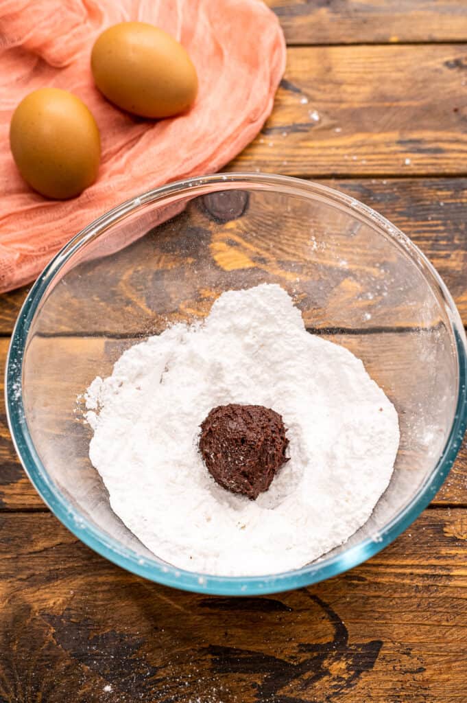 Glass bowl with powdered sugar in it and chocolate cookie dough ball.