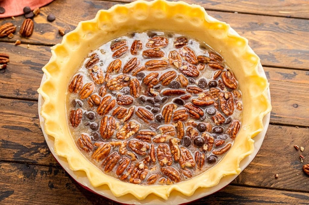 Pie crust in glass pie dish with a pecan pie filling before baking.