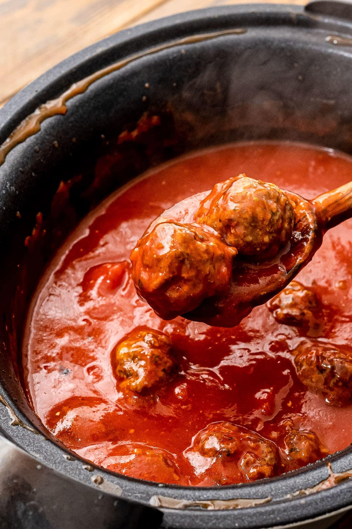 Wooden spoon scooping meatballs out of crock pot with spaghetti sauce in it.