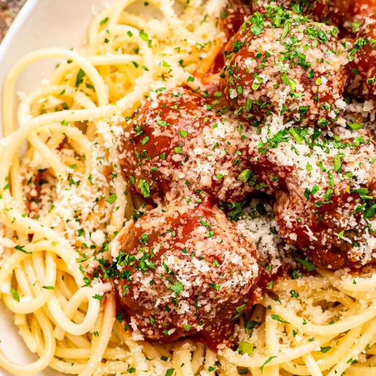 White plate with bed of spaghetti noodles topped with meatballs and sauce.