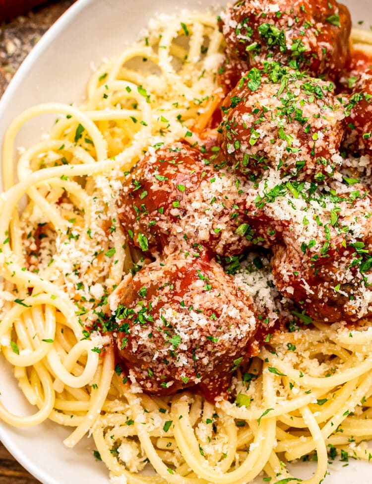 White plate with bed of spaghetti noodles topped with meatballs and sauce.