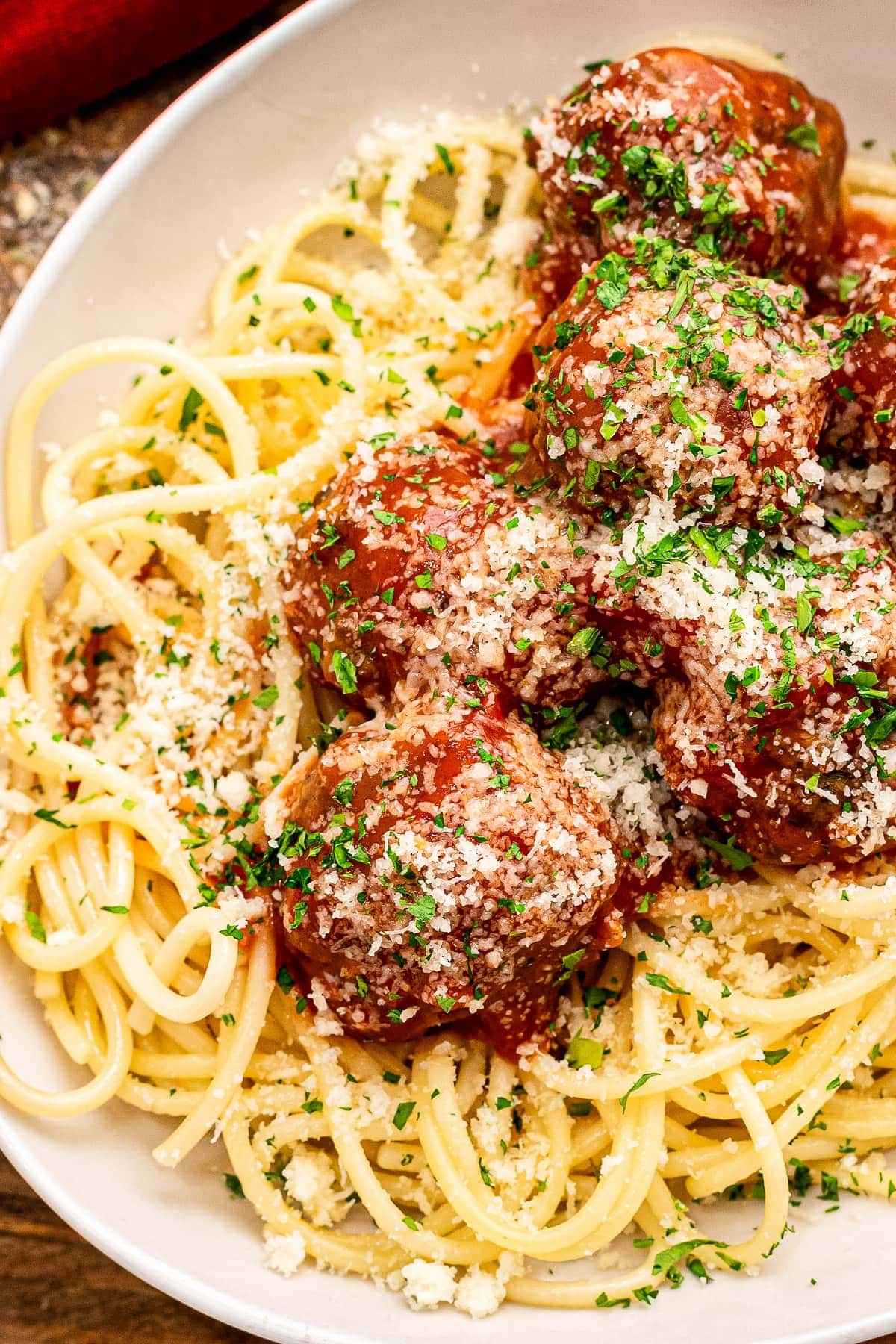 White plate with bed of spaghetti noodles topped with meatballs and sauce.