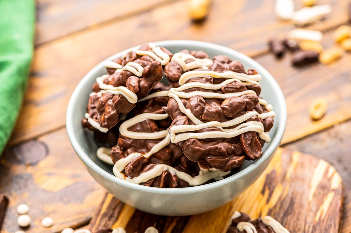 Light blue bowl with Crock Pot Chocolate Peanut Clusters drizzled with white chocolate.