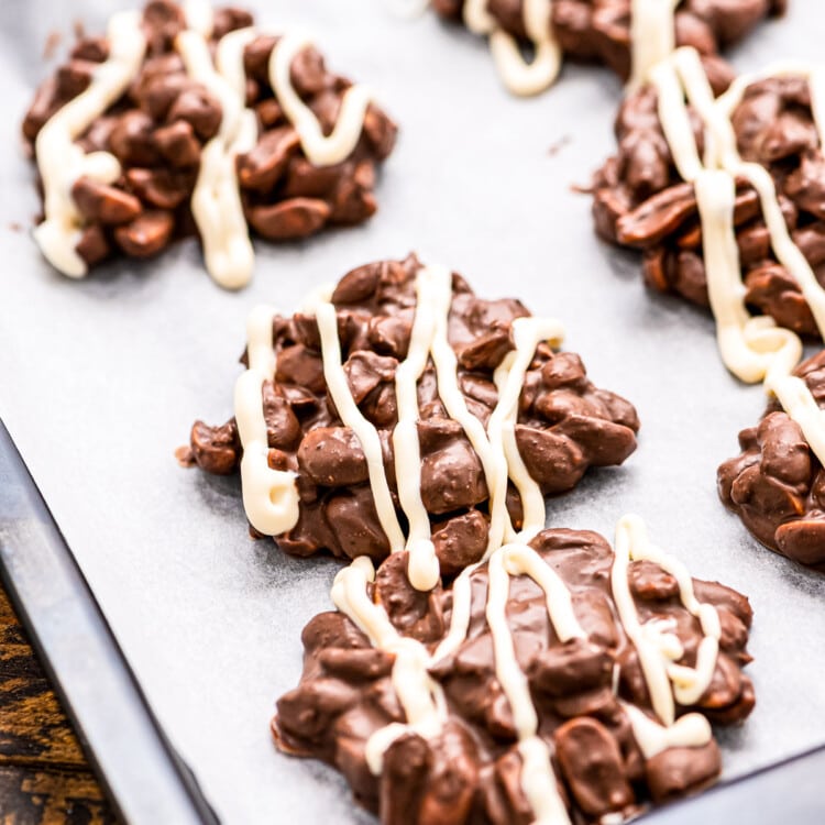 Crock Pot Chocolate Peanut Clusters topped with white chocolate on wax paper lined baking sheet