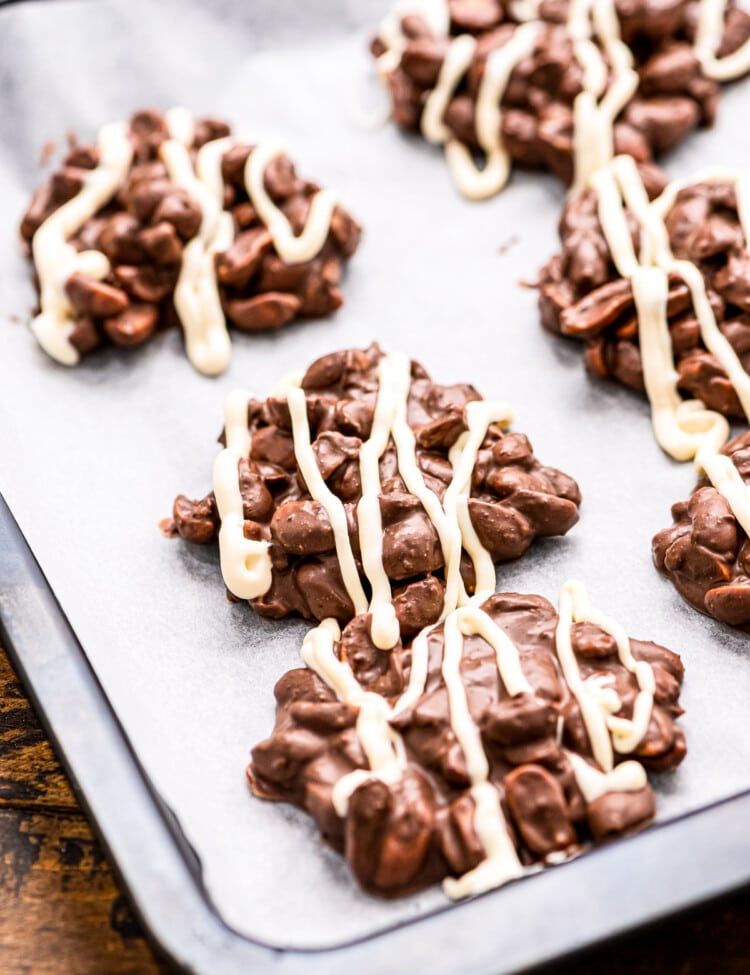 Crock Pot Chocolate Peanut Clusters topped with white chocolate on wax paper lined baking sheet