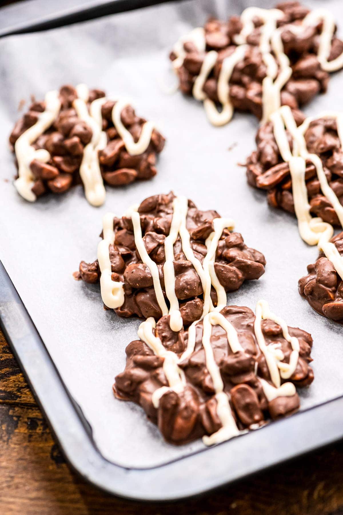 Crock Pot Chocolate Peanut Clusters topped with white chocolate on wax paper lined baking sheet