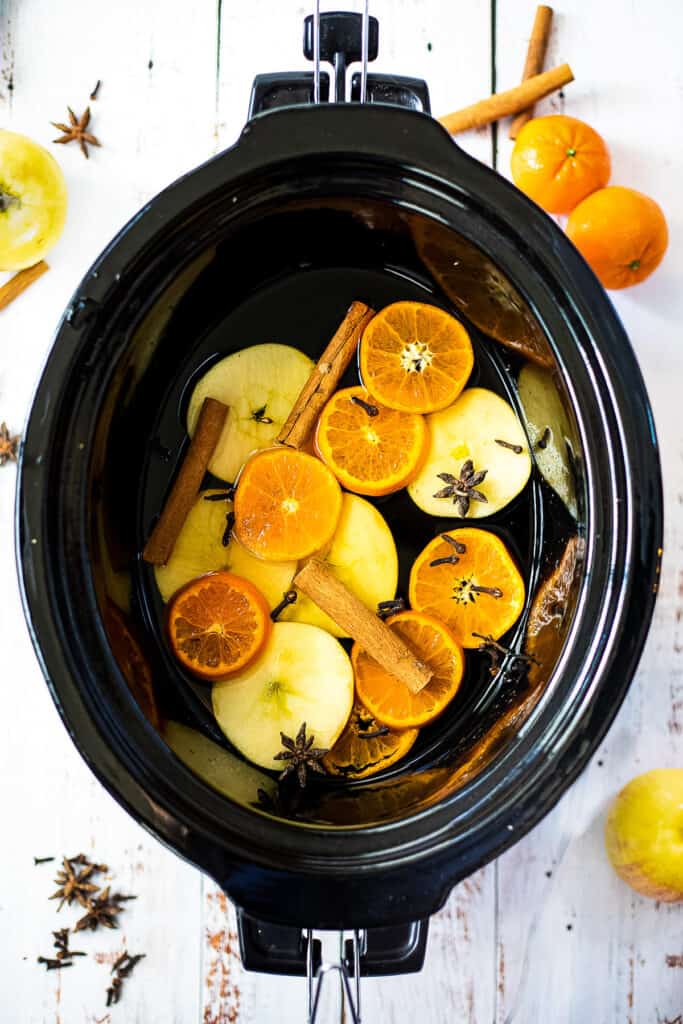 Crockpot filled with orange slices, star anise, cloves and sliced applese.