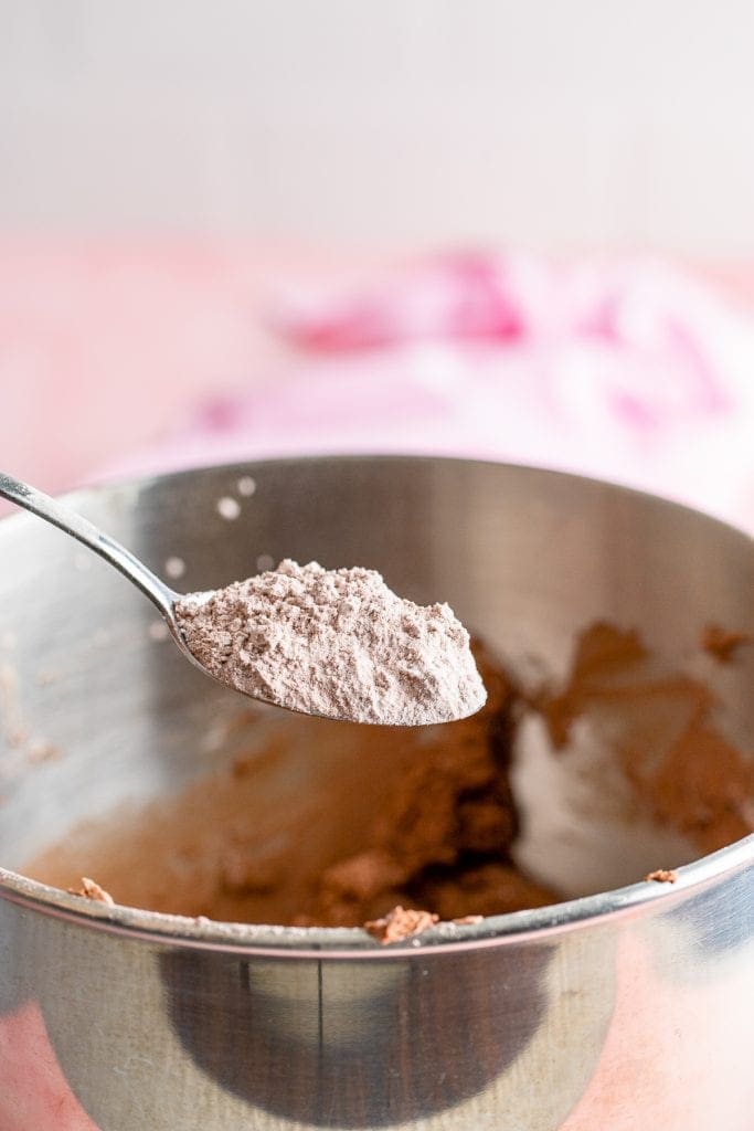 Spoon adding cocoa and powdered sugar mixture to butter in metal mixing bowl
