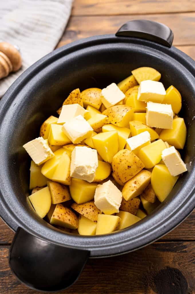 Potatoes and butter in black crock pot.